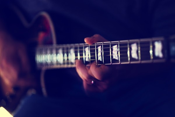 Moody close-up of a hand fretting chords on the neck of an electric guitar with pearl block inlays