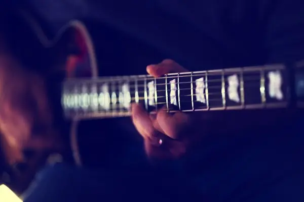 Moody close-up of a hand fretting chords on the neck of an electric guitar with pearl block inlays
