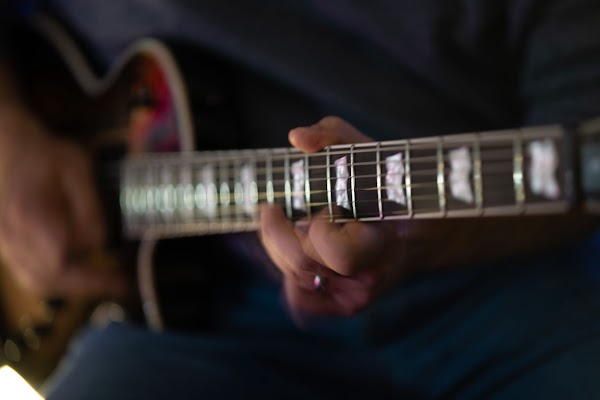 Close-up of a hand fretting chords on the neck of an electric guitar with pearl inlays