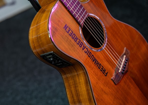 Angled close-up of an orange-toned acoustic guitar with Fresh Music Aberdeen printed across its body